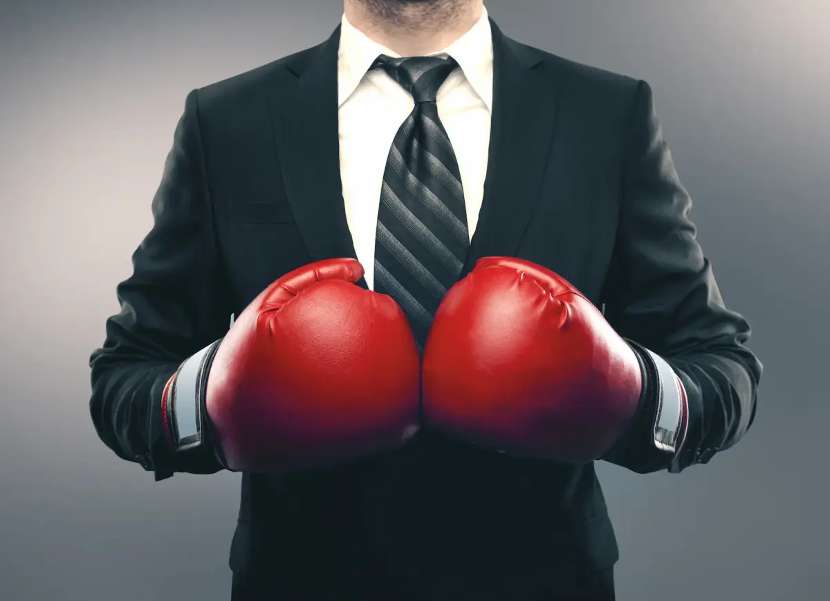 A businessman in a dark suit and tie wearing red boxing gloves